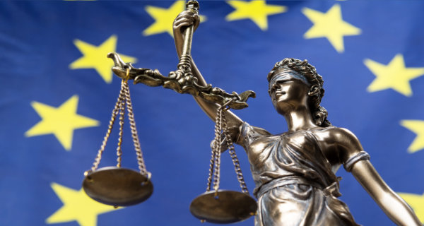Statue of the blindfolded goddess of justice Themis or Justitia, against an European flag. Foto: respiro888, Adobe Stock, 224808539